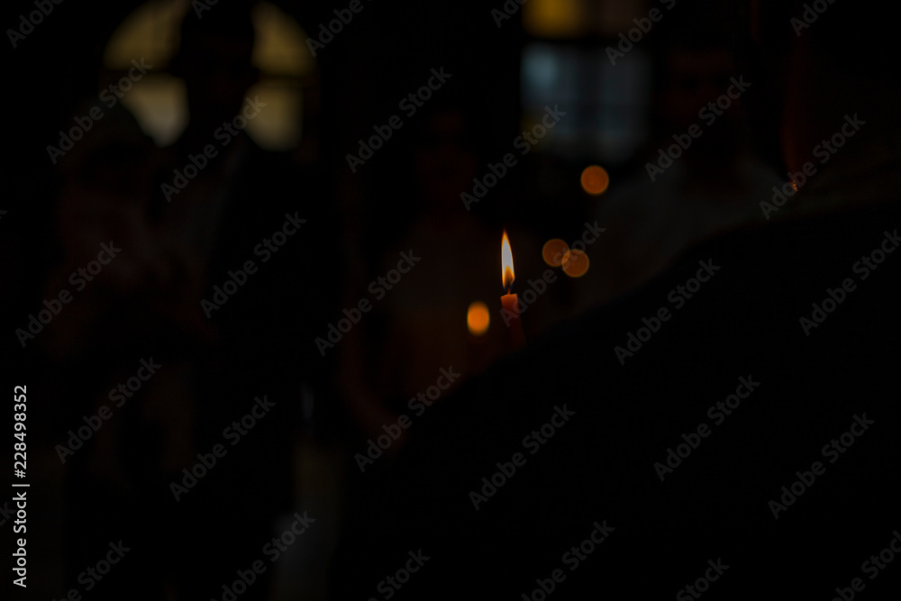 Wall mural burning candle in a Christian church. a blurred background of a church and a candle during a Christian ritual, such as a wedding or a baptism. natural light and noisy effect.looking for a dark effect.