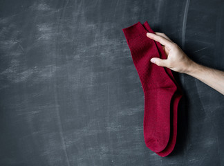 Warm red socks in the hand of a man against the background of a dark board.