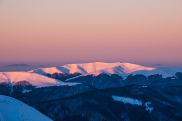 Amazing sunrise in the mountains in winter. Snow-covered peaks of mountains in the rays of the sunrise in the winter frosty morning.