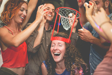 Group of happy people playing funny  basketball game inside pub cocktail bar