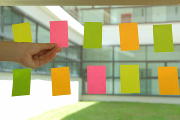 hand hold adhesive notes on glass wall. Sticky note paper reminder schedule for creative idea & business brainstorming