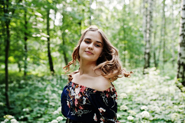 Portrait of a fabulous young girl in pretty dress with stylish curly hairstyle posing in the forest or park.