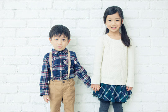 Portrait of siblings holding hands near brick wall