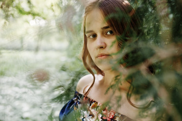 Close-up portrait of a beautiful brunette in dress next to the leaves.