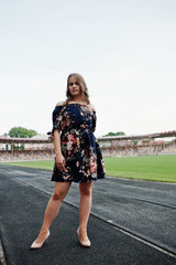 Fototapeta premium Portrait of a fabulous girl in dress and high heels on the track at the stadium.