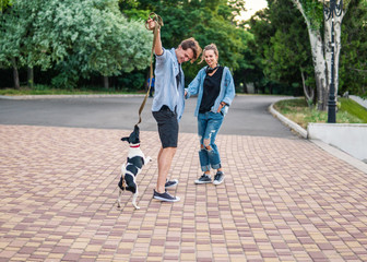 Obraz premium Lovely young hipster couple walking with dog during summer sunset. they wear jeans clothes. modern youth