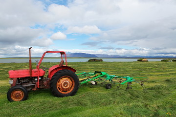 Tracteur rouge sur un champ fauché devant un lac en Islande 
