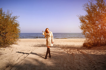 Blond woman in brown coat and black shoes with autumn background. 