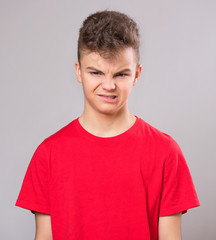 Emotional portrait of caucasian upset problem teen boy. Sad boy looking at camera. Worried  child wearing red t-shirt, on gray background.