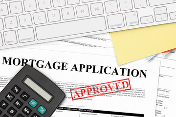 RED APPROVED RUBBER STAMP ON MORTGAGE APPLICATION WITH CALCULATOR, COMPUTER KEYBOARD, AND PAPER NOTES