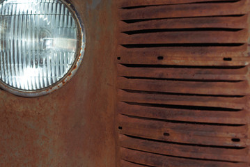 fragment of the front of a rusted vintage car, part of the radiator and headlight
