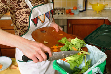 Detail of a female hand throwing organic waste in a proper bin  with kitchen in the background.