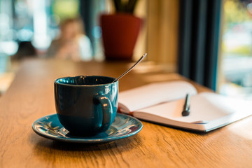 cup of coffee with spoon and open notebook with pen on wooden tabletop in cafe