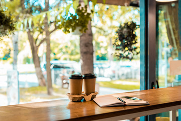 two coffee in paper cups, open notebook with pen on cafe counter