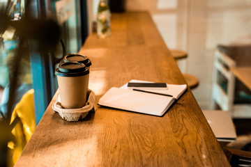 two disposable coffee cups, open notebook with pen on cafe counter