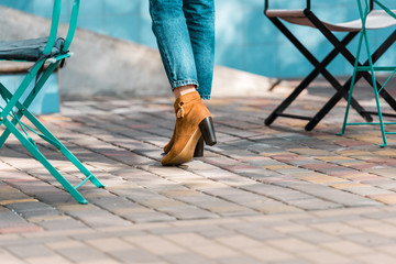 low section of woman in jeans high heels standing on street near cafe chairs