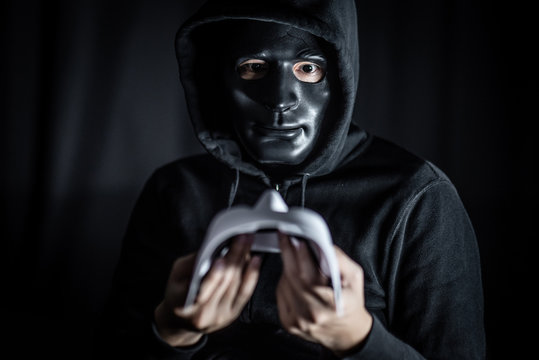 Mystery hoody man wearing broken black mask holding white mask. Anonymous social masking. Major depressive disorder or bipolar disorder. Halloween concept