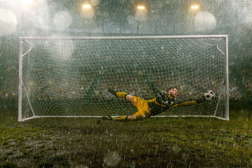 Dirty goalkeeper in flight catch the ball. Professional night rain stadium with football goal....