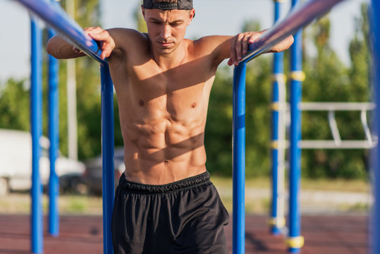 Image of young Caucasian muscular male doing pull ups exercises on horizontal bar outdoors. Athletic runner training hard at sunny day outside on the bar. Sportsman working out on crossbar.