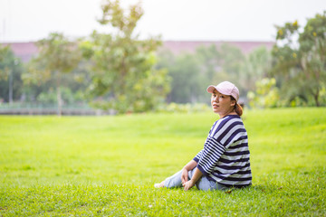 Fototapeta premium Asian woman sitting on the grass looking back to the camera in the park 