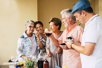 People group with mixed ages and sex  having fun together in friendship for a dinner or lunch. Men playing with phone and technology. Smiles and cheerful concept