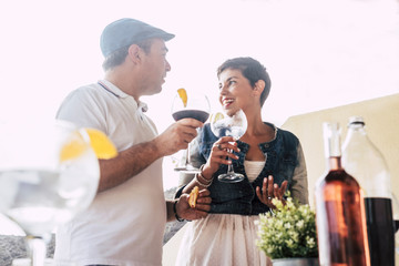 Happy adult couple enjoy and have fun smiling together outdoor in a bar or home drinking a big glass cocktail together. White clear sky in background