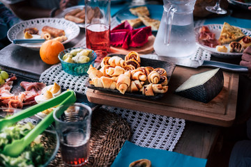 Real scene of a wooden table at home or bar  restaurant full of food and drinks to enjoy the night together with friends celebrating.