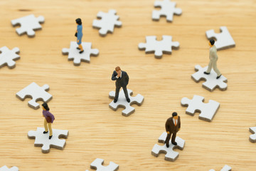 Miniature people businessmen standing on white Jigsaw. The concept used in selecting personnel to participate in the organization. with copy space.