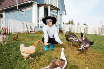 A young girl feeds domestic birds, ducks, hens, geese, turkeys in the yard of a rural house. Farmer, agriculture.