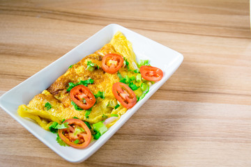 A photo of an omelette with cherry tomatoes, parsley. and grated cheese, shot from above on a rustic wooden texture with a place for text