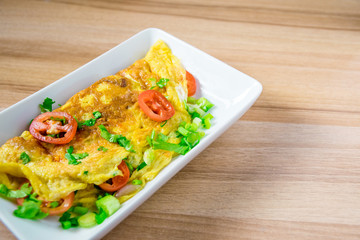 A photo of an omelette with cherry tomatoes, parsley. and grated cheese, shot from above on a rustic wooden texture with a place for text
