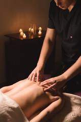 Fototapeta premium Men's hands make a therapeutic neck massage for a girl lying on a massage couch in a massage spa with dark lighting. Close-up. Dark Key