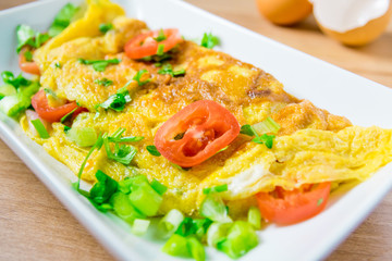 A photo of an omelette with cherry tomatoes, parsley. and grated cheese, shot from above on a rustic wooden texture with a place for text