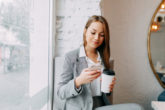Young blogger girl with coffee sitting and working in a cafe. Bright portraits in the coffee shop, smiles and happy eyes. Business woman, strict style
