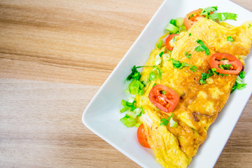 A photo of an omelette with cherry tomatoes, parsley. and grated cheese, shot from above on a rustic wooden texture with a place for text