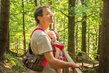 Obraz premium Father with a sleeping baby in a backpack for a walk in the woods.