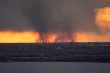 environmental pollution problem of fire on dry grass with smoke onthe horizon inflated by a strong wind during the sunset