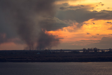 Naklejka na ściany i meble environmental problem of fire on dry grass with smoke onthe horizon inflated by a strong wind during the sunset