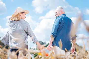 Fototapeta premium Lovely look. Blonde-haired wife wearing nice beige hat looking at her handsome husband after gathering harvest