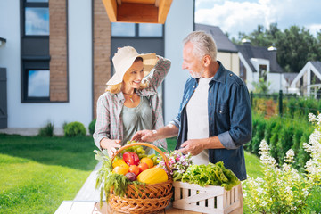 Helpful husband. Caring loving husband helping his beautiful busy wife standing outside and cooking salad