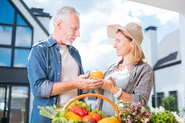 Fruits and vegetables. Stylish handsome man wearing denim shirt bringing fruits and vegetables his beautiful beaming wife