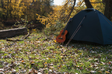 The guitar near the tourist tent on the background of the river and forest on sunny warm day; The...