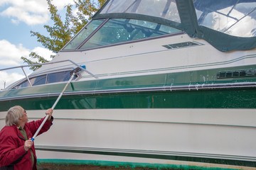 Caucasian man washing power boat with long handled brush