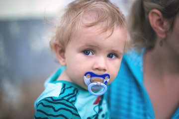 Little cute boy with a baby pacifier in his mouth in his mother's arms