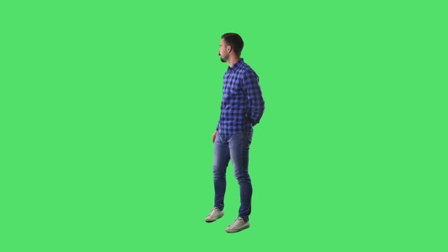 Displeased young man showing thumbs down and scolding finger gesture. Full body isolated on green screen background. 