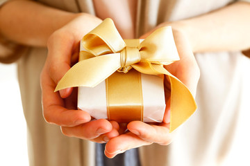 Young casual woman wearing pink shirt and long beige cardigan holding a beautiful present in shiny...
