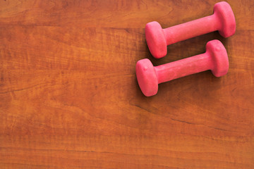 Pair of pink dumbbells on wooden background.