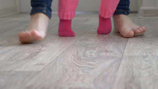 feet of child and mother walk along floor in nursery, small child learns to walk with mother. close-up.