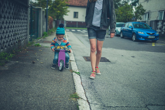 Mother walking in the street with toddler on tricycle