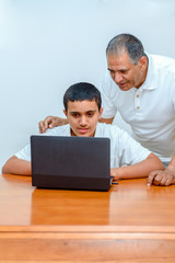 Senior Father and teenage son using laptop. Boy and dad with deeper skin tones working with computer. Happy family old grandfather and grandson on laptop.Elderly teacher trainer and teen pupil boy.